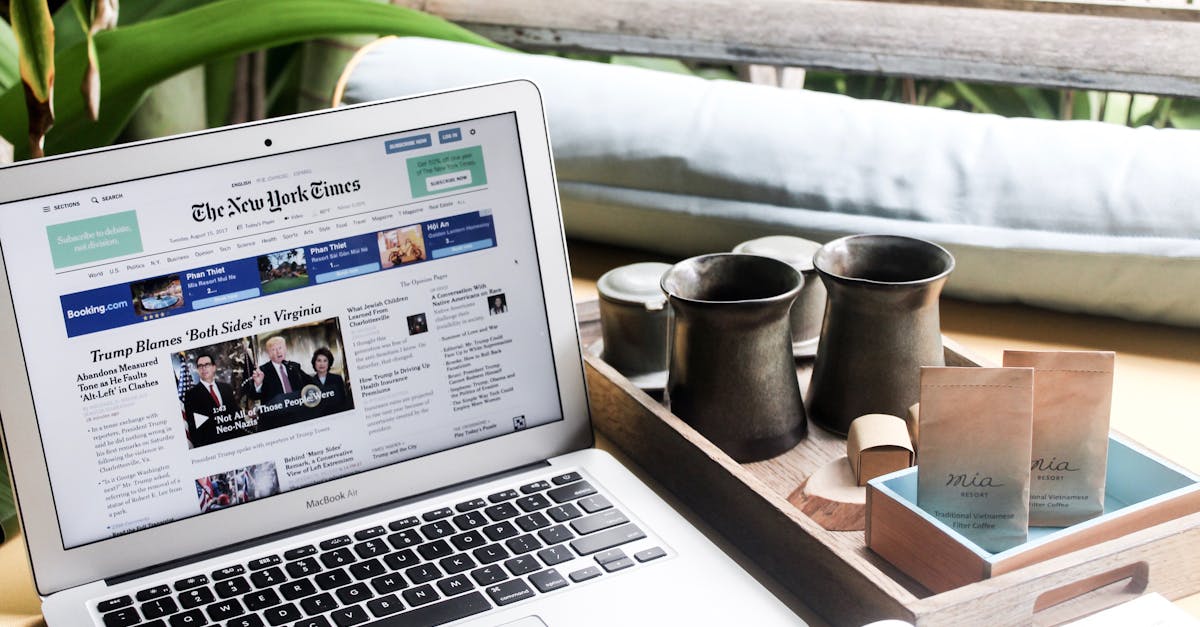 High angle of modern laptop with news on screen placed on table next to tin cups